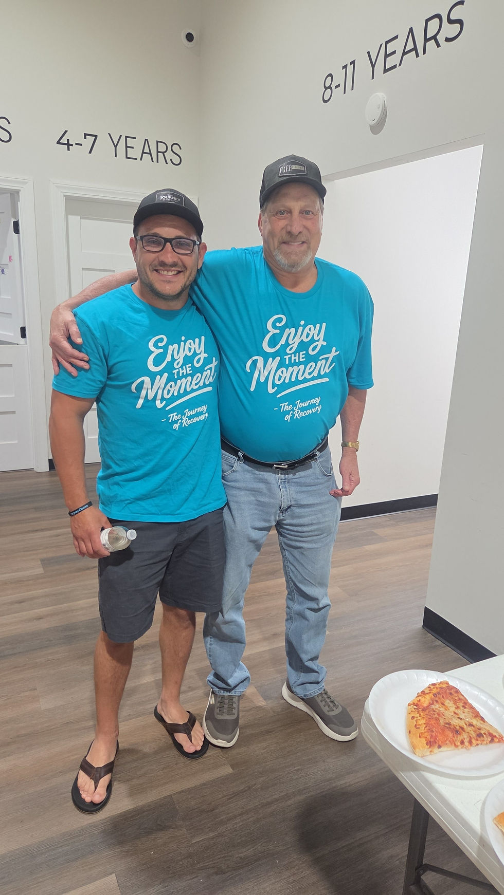 Two adult men wearing teal Journey of Recovery T-shirts