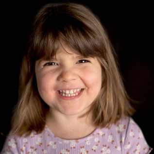 A young girl smiles during fine art school pictures against a black backdrop in Pittsburgh, PA.