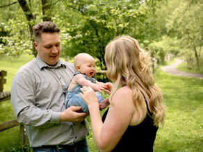 A young baby boy is smiling and reaching for his mother while his dad is holding him at Beechwood Farms Nature Reserve.