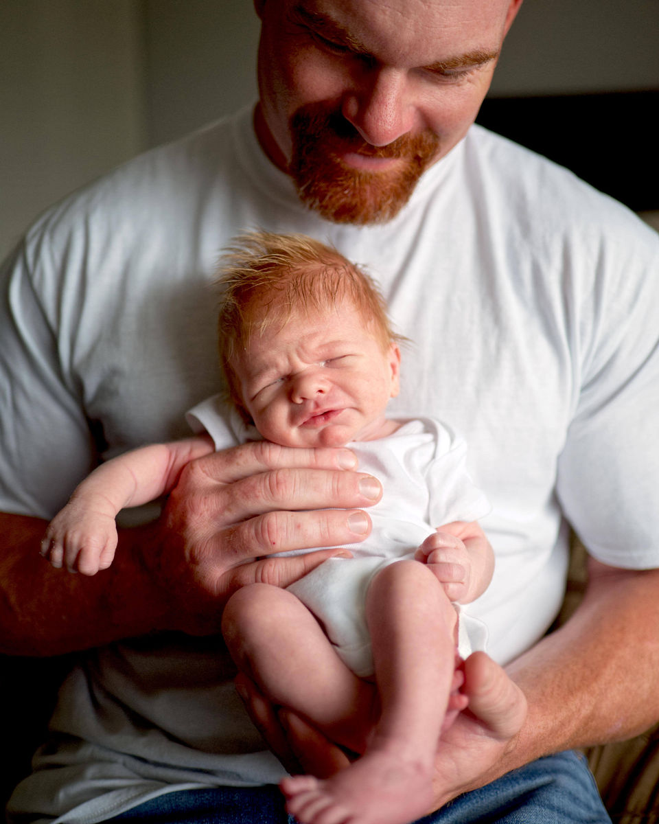 A father is holding his newborn baby boy while the newborn is sleeping.