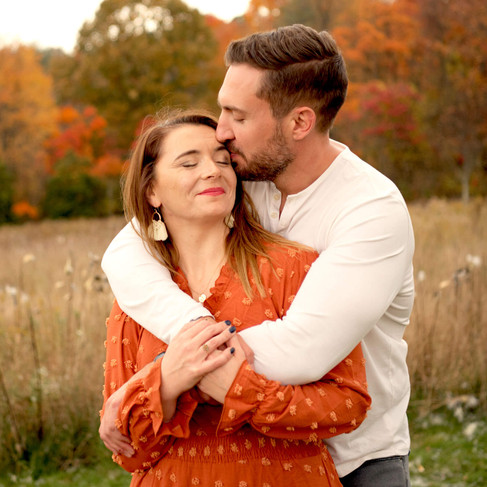 A husband hugs his wife from behind in a beautiful field in autumn.