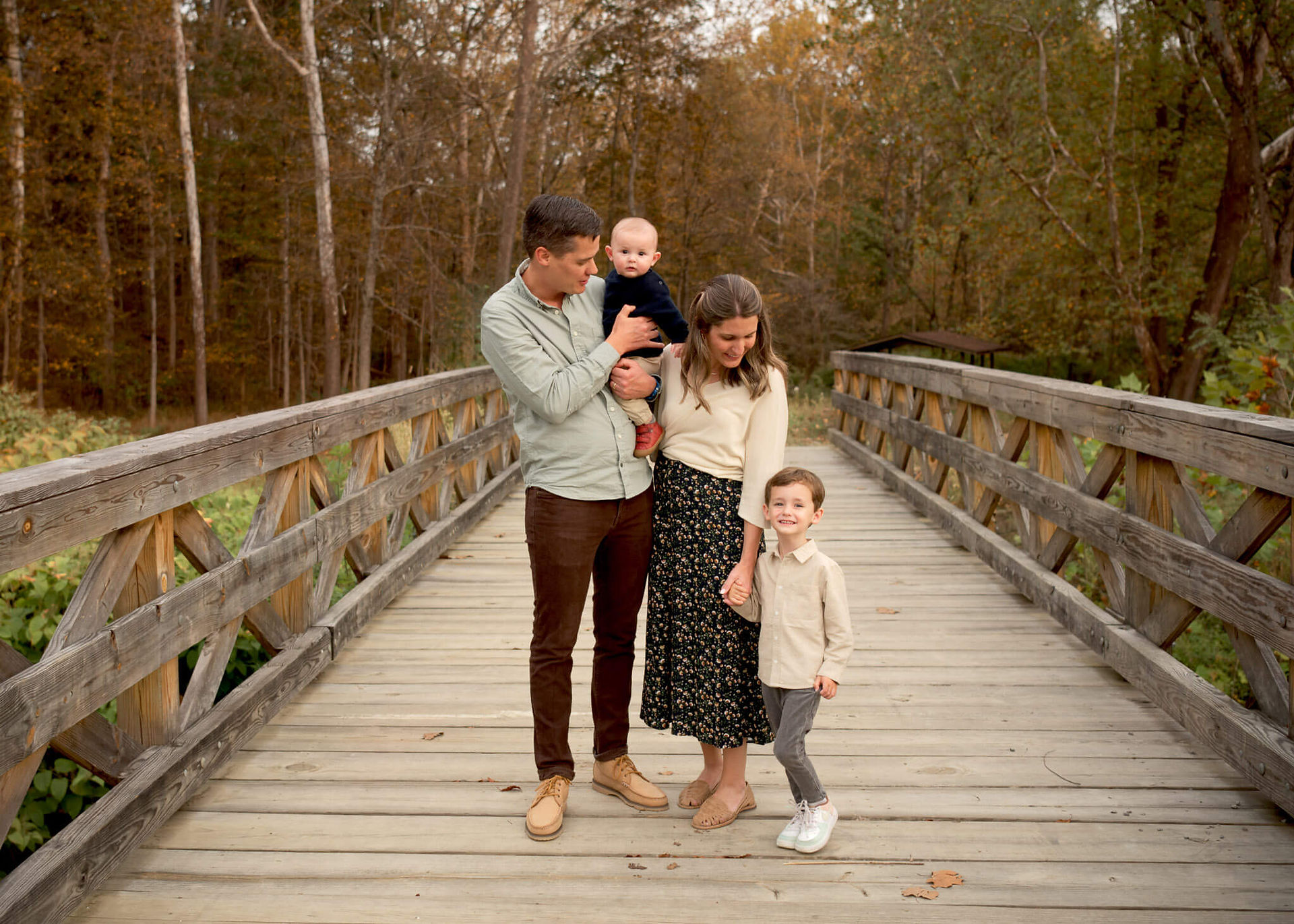 A family of four stand on a bridge and look at each other during family photos.