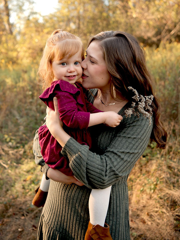 A mother kisses and holds her daughter while they stand in a field at Sewickley Heights Borough Park.