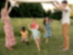 Four kids are joyfully running under a blanket their parents are holding.