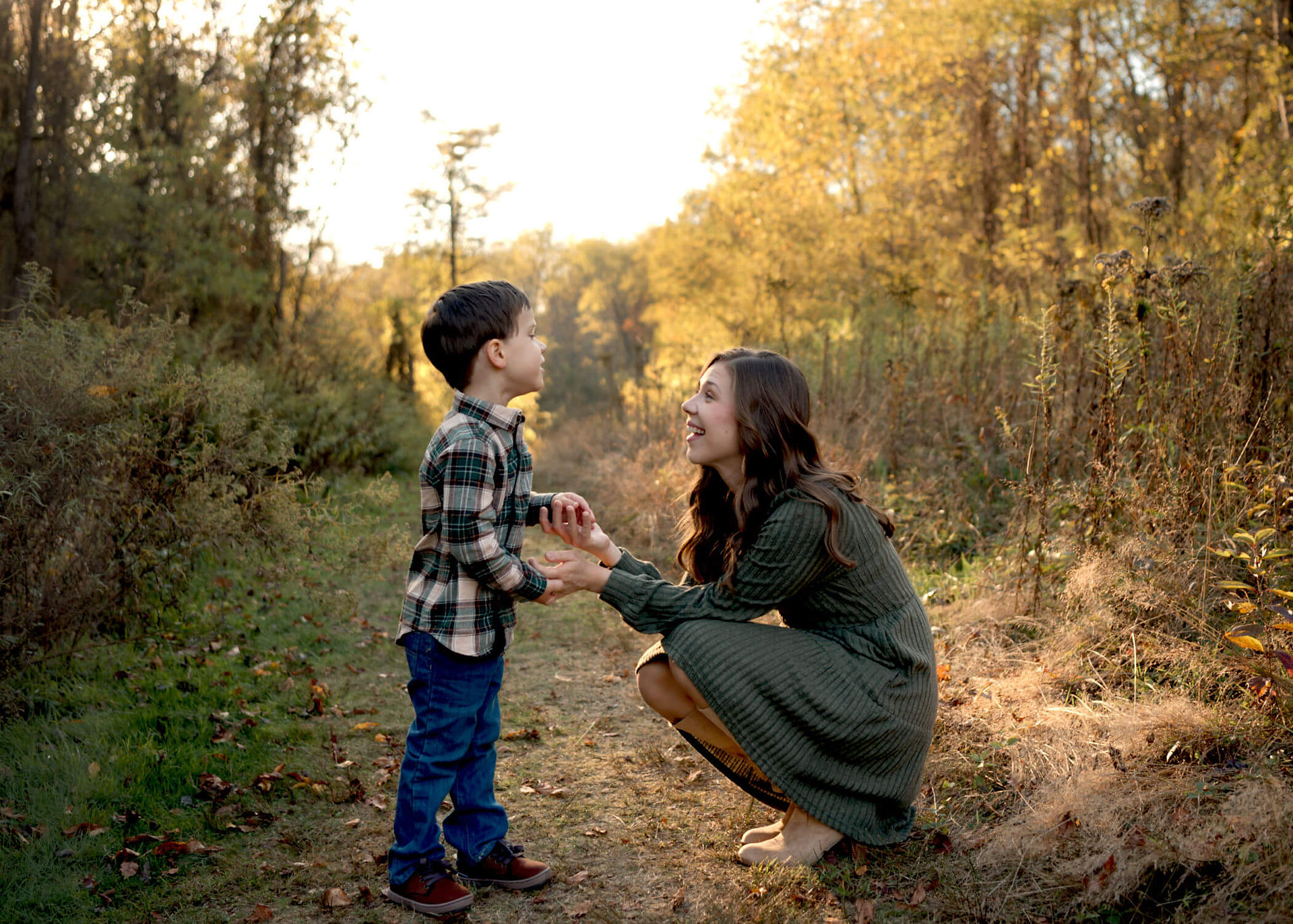 A mom crouches next to her son and smiles at him outside. 