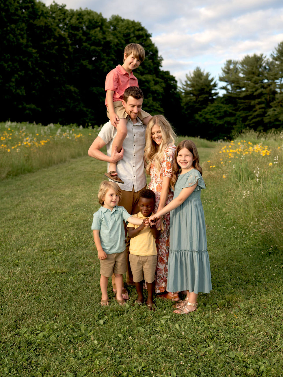 A family of six are standing together in a field and smiling at each other during gorgeous golden hour light.