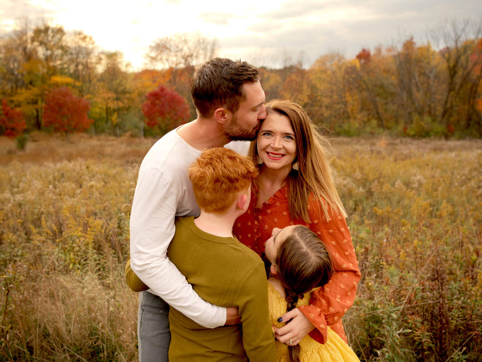 A mother smiles while her family hugs her in the gorgeous fall golden-hour light.