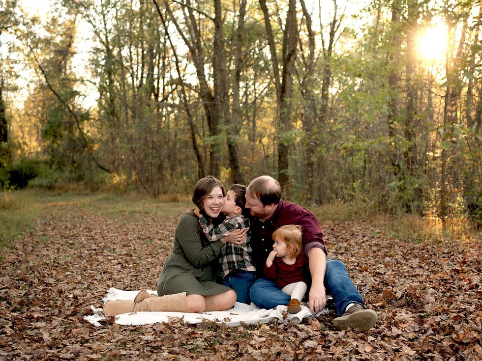 A family of four sits under trees and on top of fallen fall leaves while they interact with each other at Sewickley Heights Borough Park.
