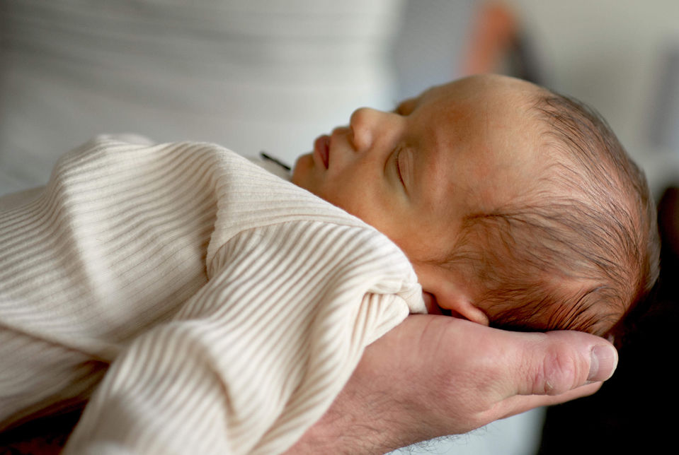 A newborn baby girl is sleeping in her father's arms.