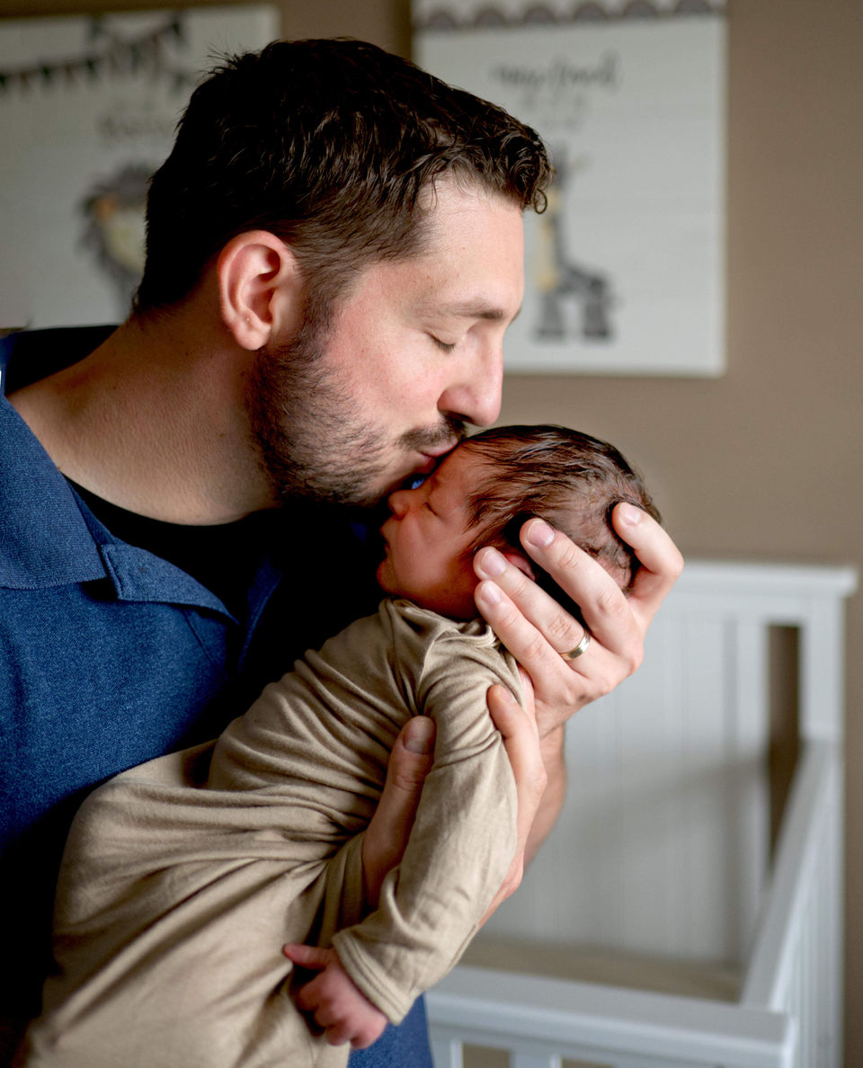 A father is holding his newborn son and kissing him on the forehead.