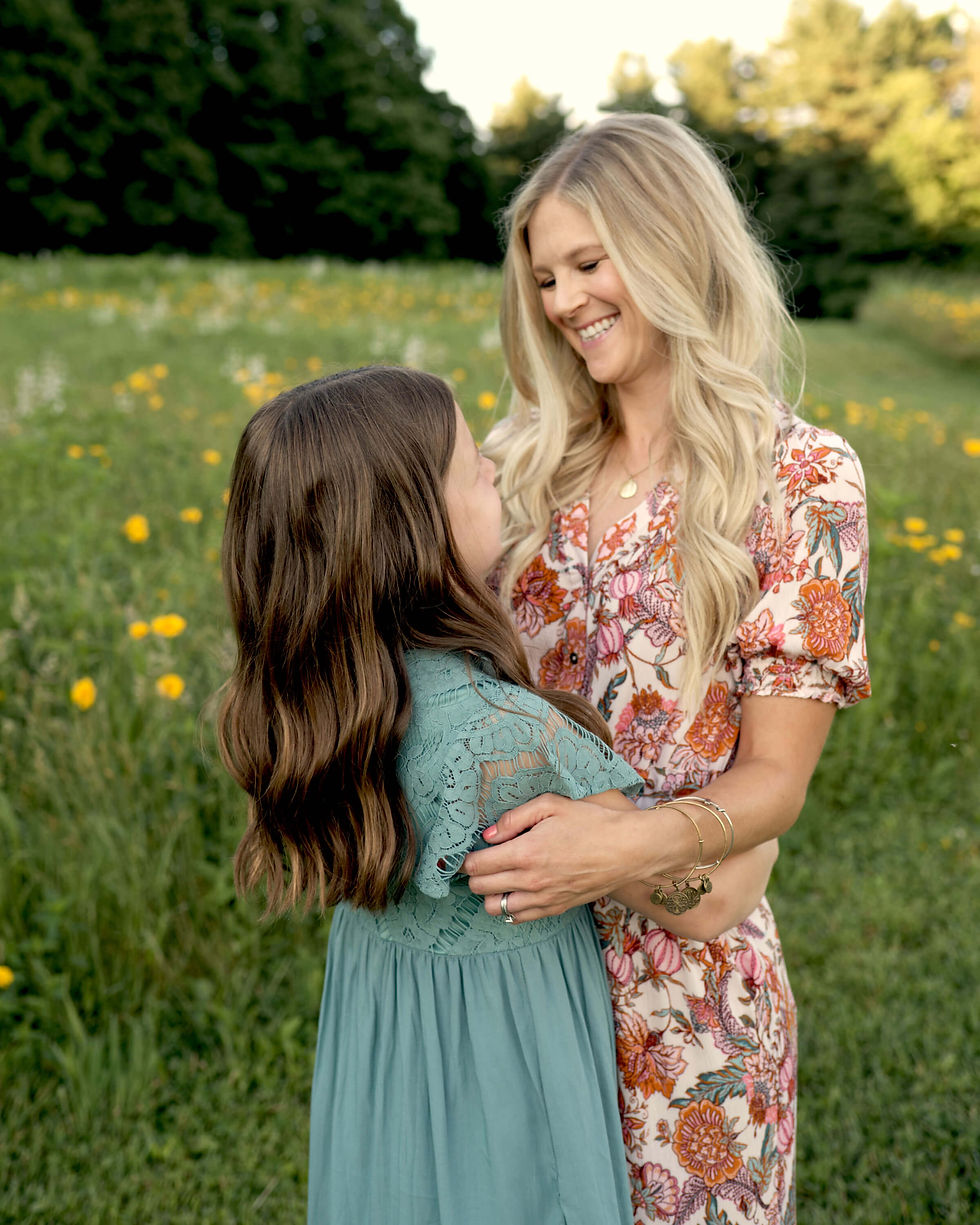 A mother is lovingly smiling at her daughter while they are embracing outside during golden hour..