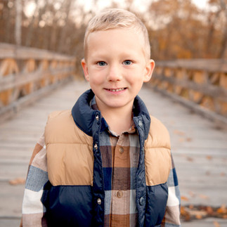 A boy stands and smiles on a bridge during family photos. 