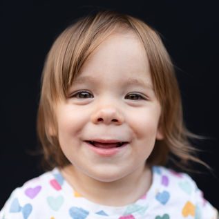 A young girl smiles during fine art school pictures against a black backdrop in Pittsburgh, PA.
