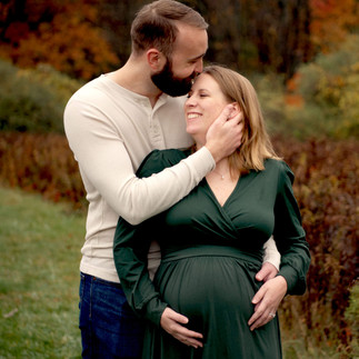 A pregnant mother laughs with her partner against a beautiful fall backdrop.