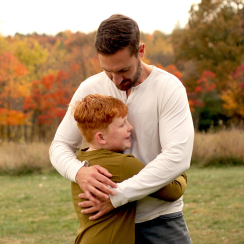 A father hugs his son in a field with fall colors surrounding them.