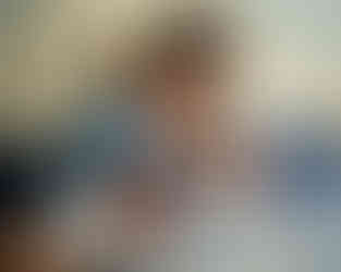 A mother is holding her newborn baby boy on a bed while the big brother looks over the mother's shoulder.