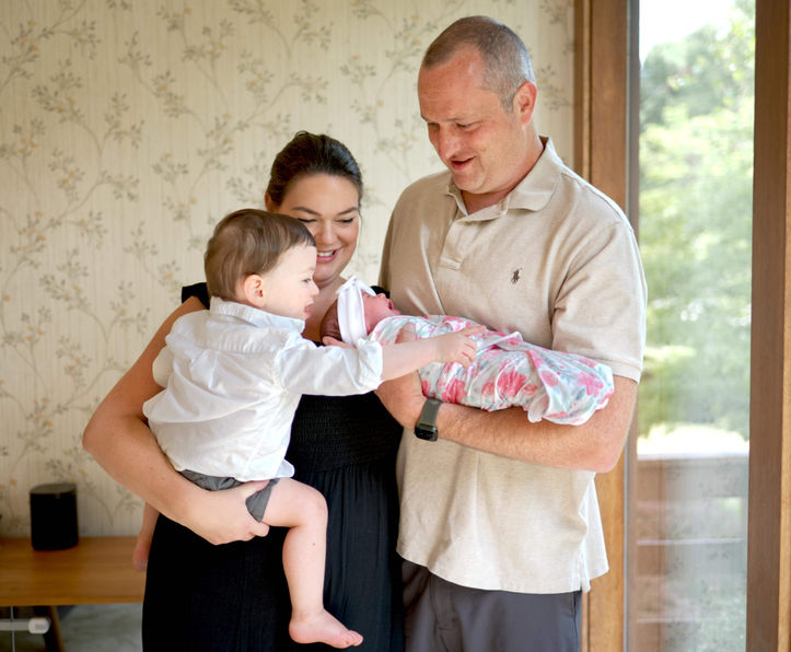 A family is interacting with a newborn baby girl in their home.