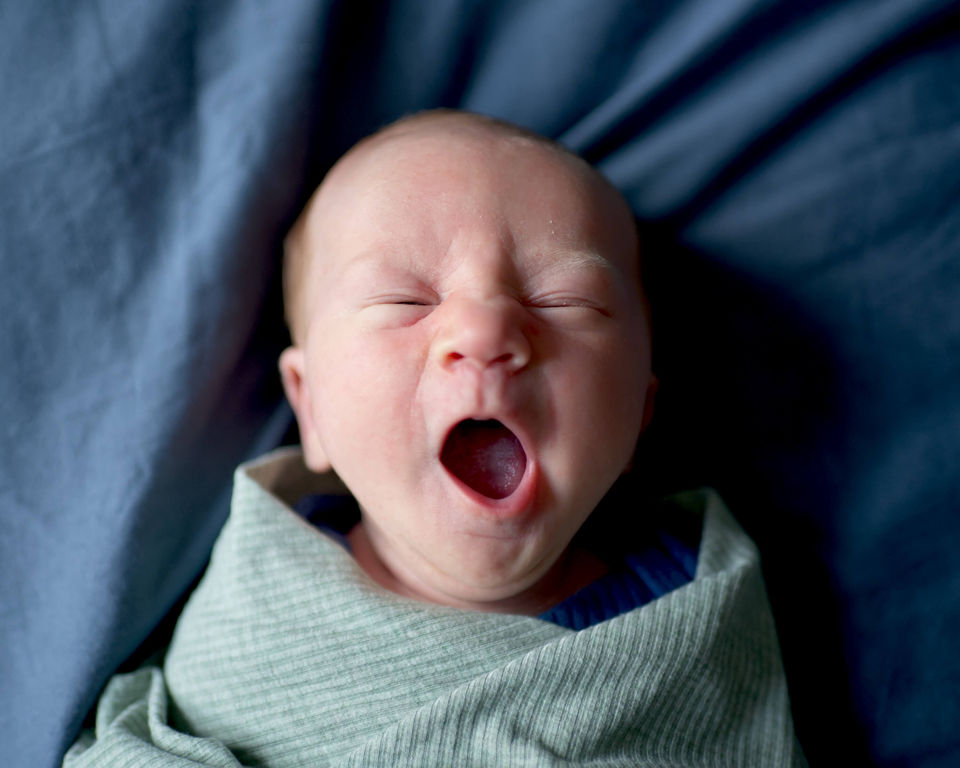 A newborn baby boy yawning sweetly while swaddled.