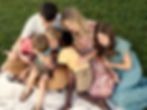 A family of six is cuddling together in the grass while one young boy smiles.