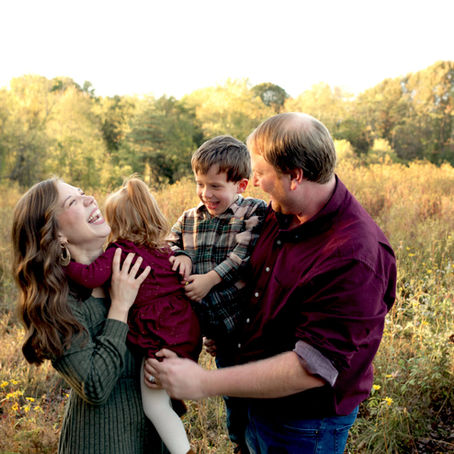A family of four laughing and tickling each other while standing in Sewickley Heights Borough Park. 