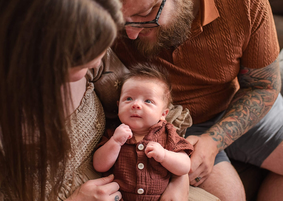 A newborn boy gazes at his mother while the dad sits next to them on the couch during a newborn session in Pittsburgh, PA.