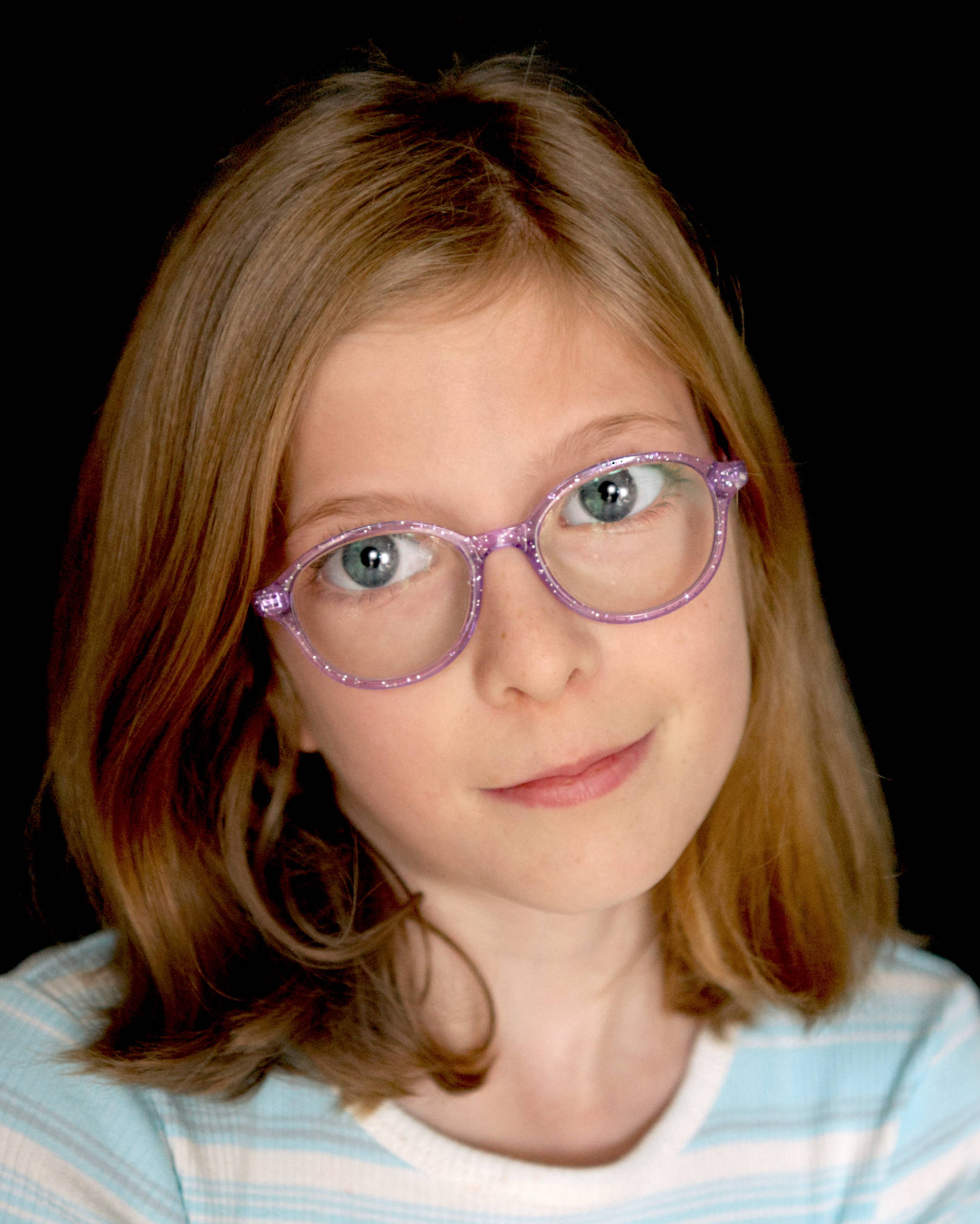 A girl smiles during school pictures while smiling against a black backgound.