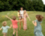 Three kids are running towards their parents and laughing in a field.