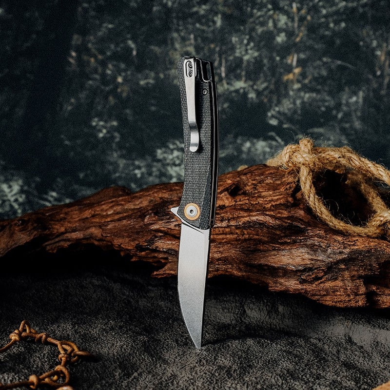 Folding utility knife standing vertically on blade tip with pocket clip and textured handle visible against a rustic wood and