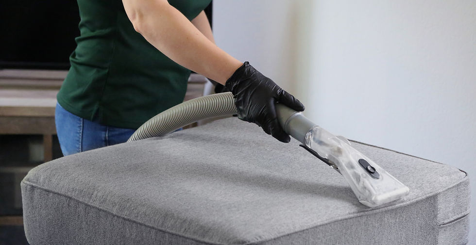 a woman in a green shirt and black gloves vacuuming a gray ottoman_edited.jpg