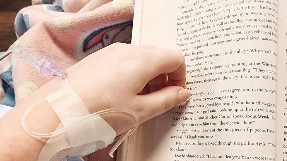 Ava's hand with an IV reads a book. Text is visible on the page. Background shows a colorful patterned blanket, evoking a calm mood.