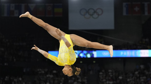 Rebeca Andradre hangs upside down in the air was she competes on the beam with both legs and arms outstretched