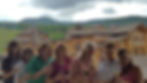 Seven women smiling, holding wine glasses in front of a lodge with mountain views. Overcast sky, relaxed and cheerful mood.
