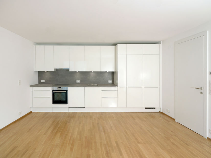 Moderne weiße Einbauküche mit grauer Rückwand in einer Wohnung der Eduard-Pötzl-Gasse 4.