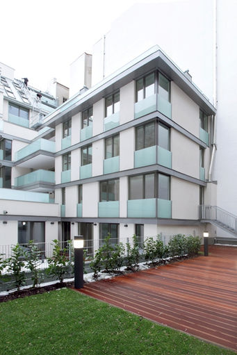 Modernes Wohngebäude in Wien mit klarer Linienführung, Glasbalkonen und Gartenbereich mit Holzterrasse – stilvolles Immobilienprojekt der LENIKUS Gruppe mit Fokus auf urbanes Wohnen und moderne Architektur.