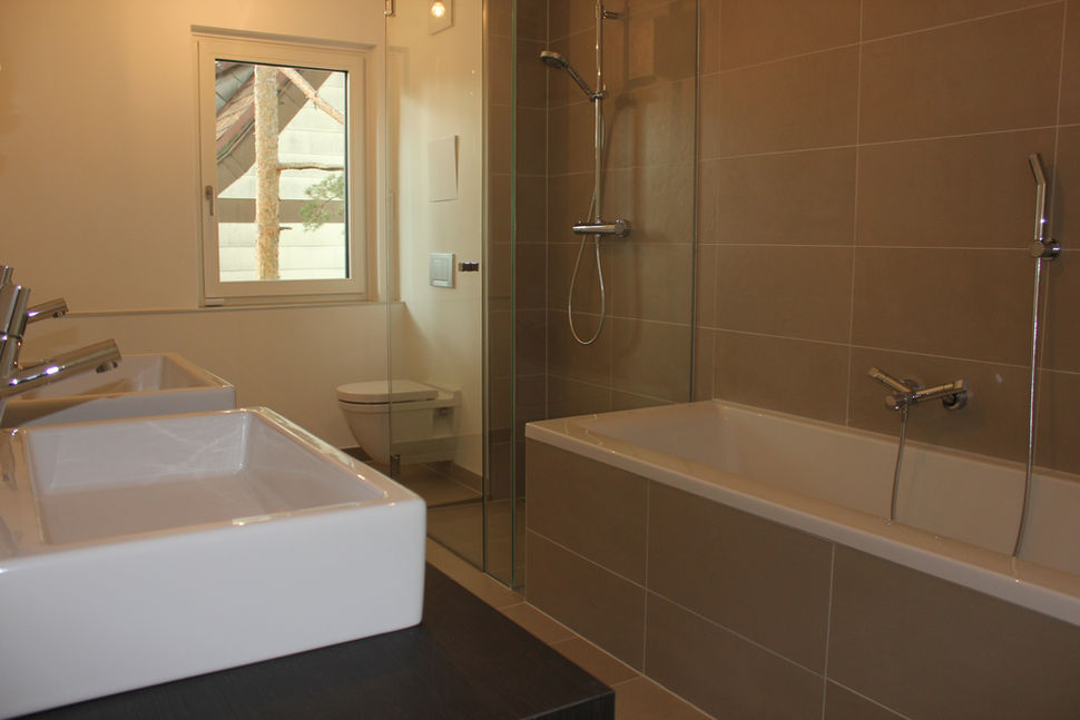 Helles Badezimmer mit zwei Waschbecken, bodengleicher Dusche und Badewanne in modernem Beige-Ton.