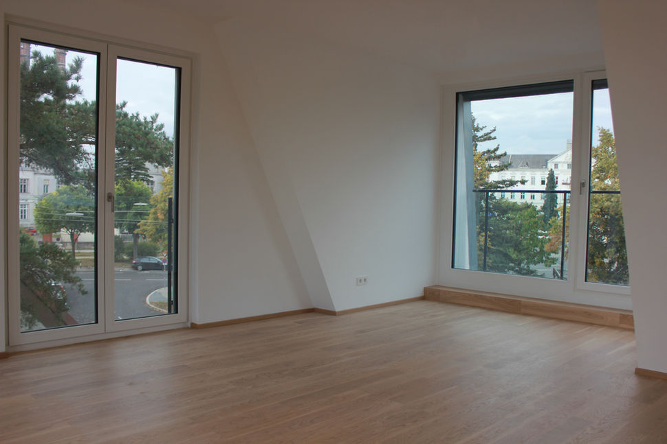 Helles Zimmer mit großen bodentiefen Fenstern und Blick auf umliegende Wohnhäuser und Bäume.