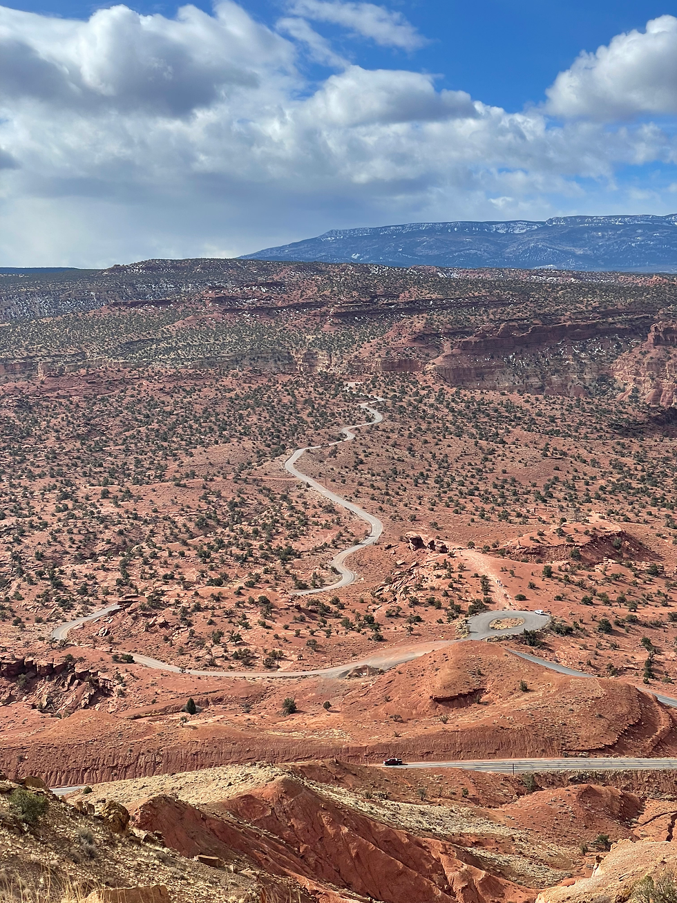 A windy road disappearing into the distance across a desert valley covered in shrubs.