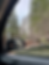 A woman in the sideview mirror of a car looking at passing trees and mountains out the window. 