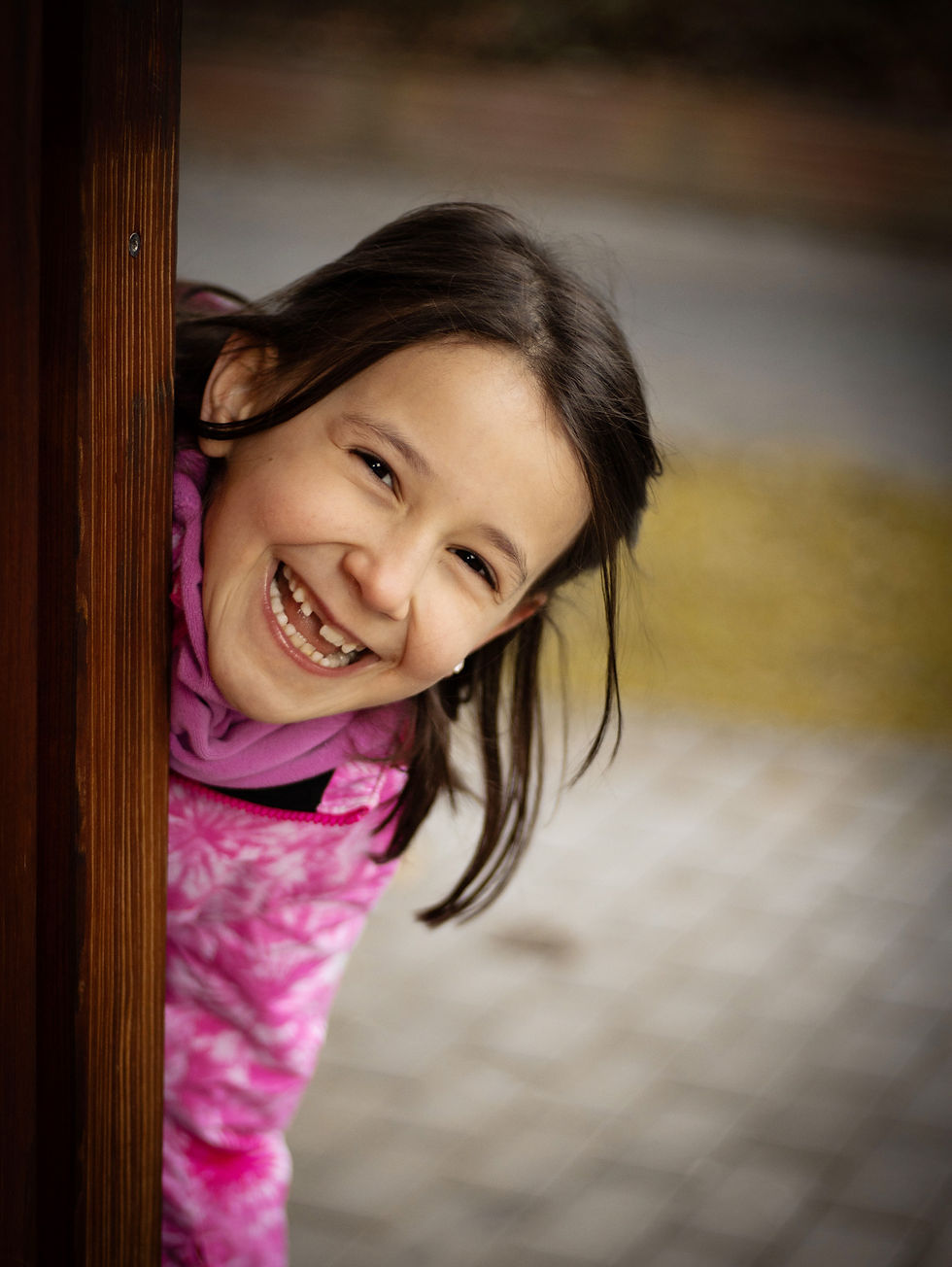 Authentische Kitafotografie in Groß-Gerau. Mädchen versteckt sich hinter einer Holzwand.