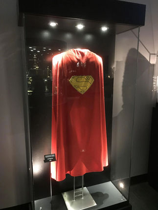 Capa roja de Superman exhibida en una vitrina, con el escudo amarillo aplicado en la espalda.