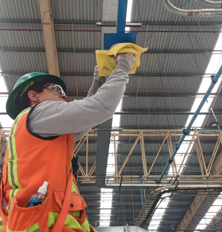 Técnico realizando limpieza y mantenimiento preventivo a cámara de seguridad en nave industrial.
