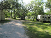 RV recreational vehicle motor home in far distance. Bumoer pull camper trailer with slide out. View down main road drieveway in Alexsandra Rv Park.