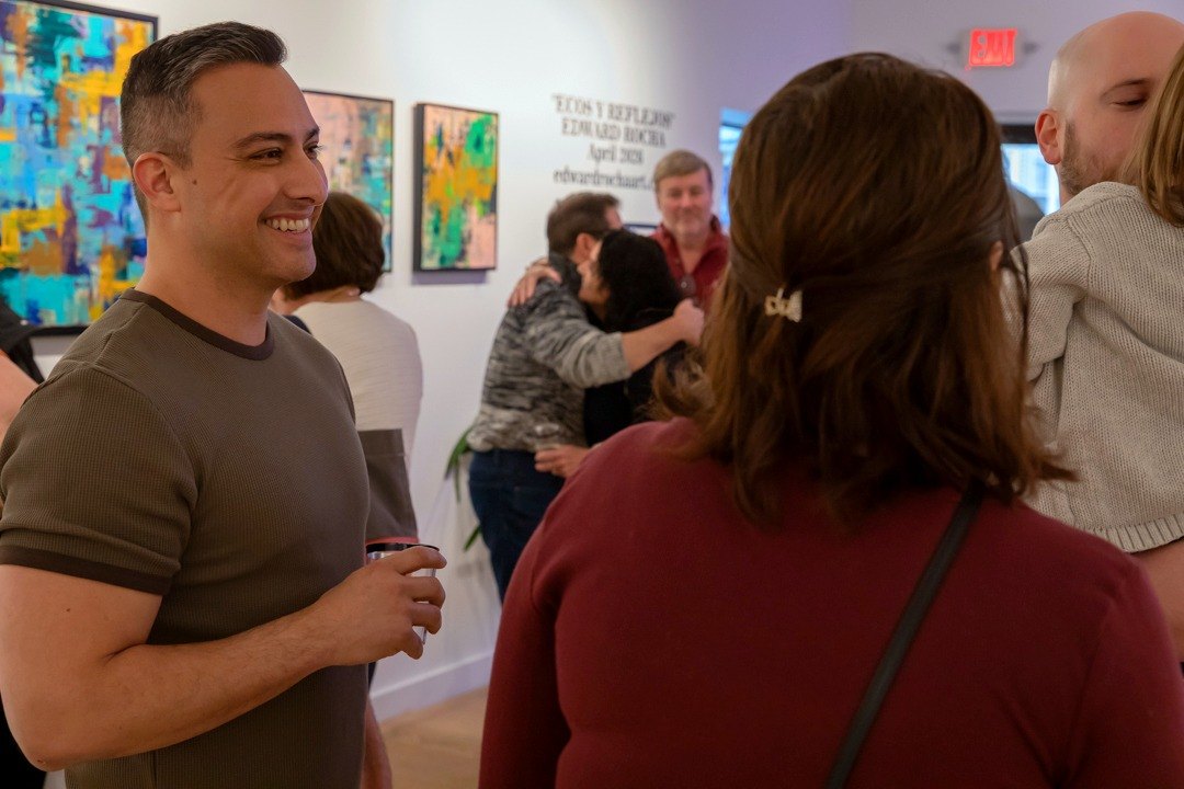 Edward Rocha smiling in conversation with a guest in the gallery