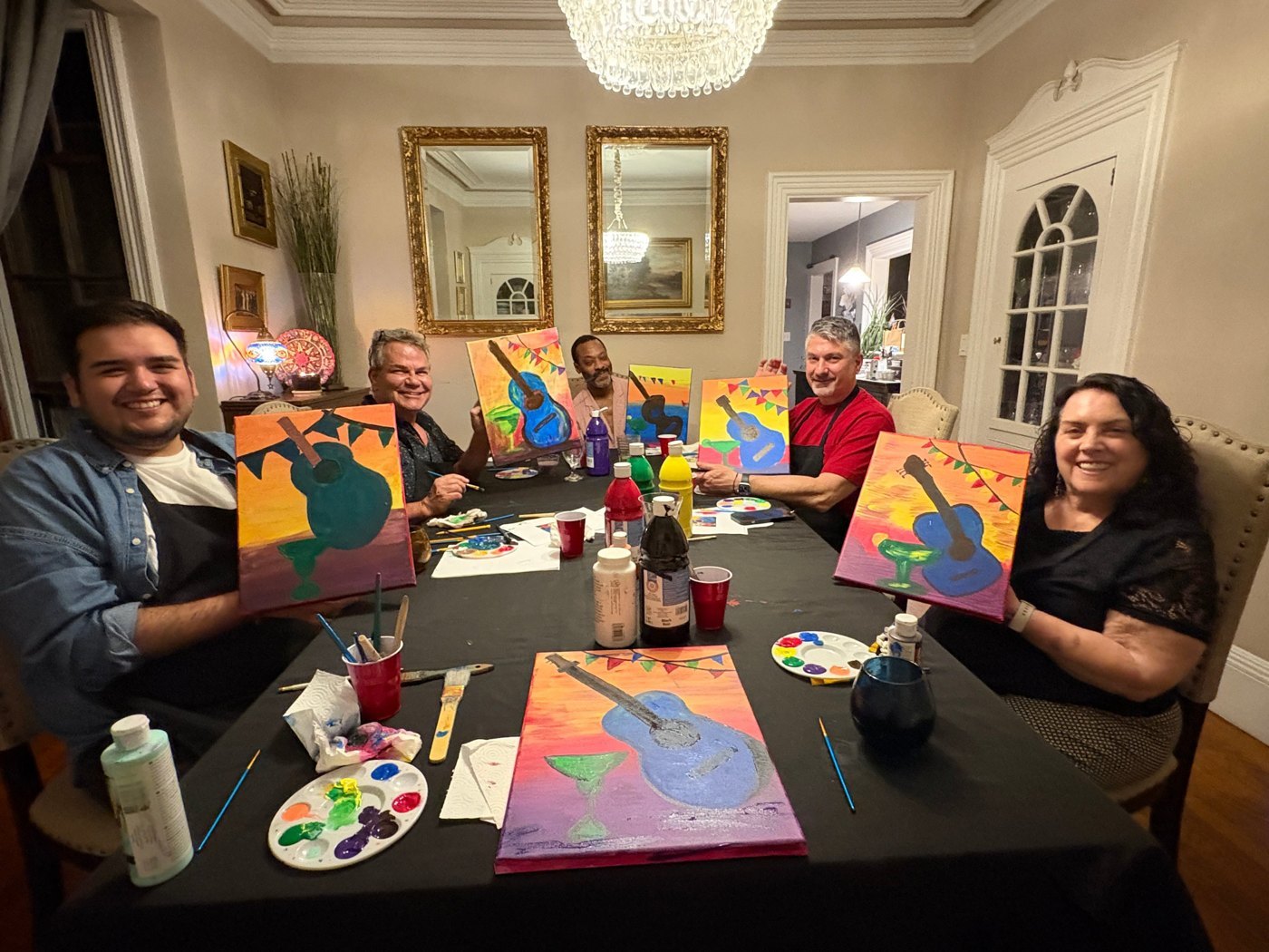 A paint and sip around a dining table, guests holding guitar paintings