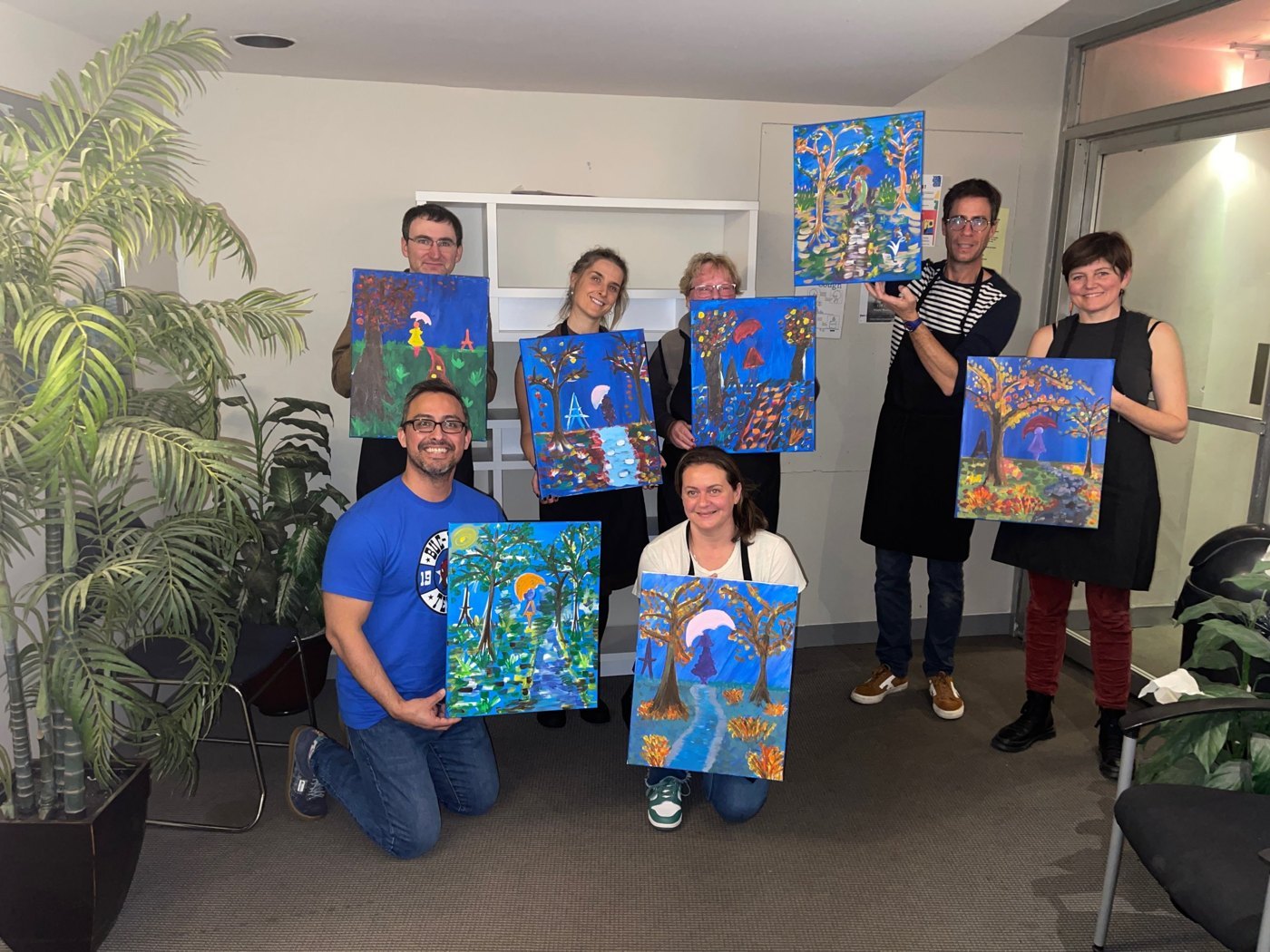A workplace paint and sip group holding their tree paintings