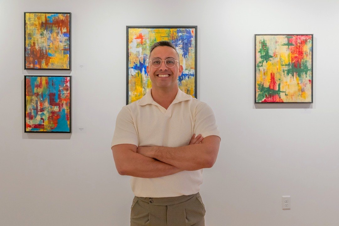 Edward Rocha, arms crossed, in front of his paintings