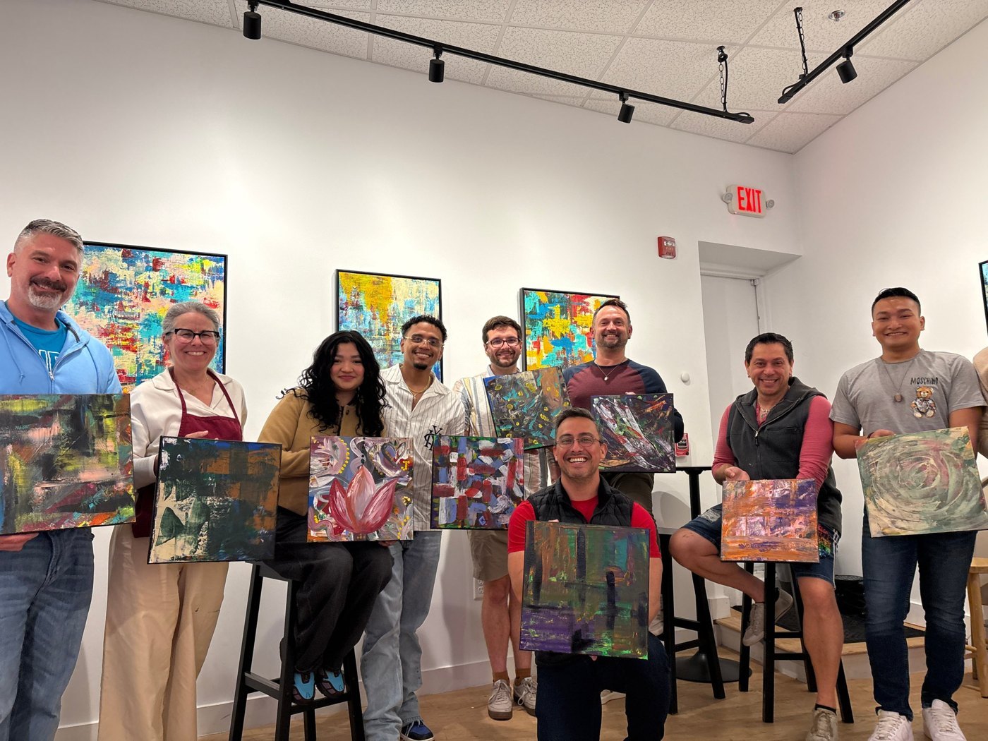 A paint and sip group holding up their finished abstract canvases in the gallery