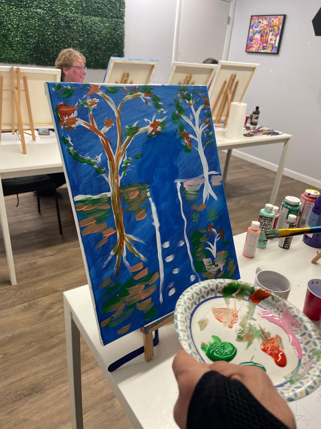 A canvas in progress on a tabletop easel, with a paint palette