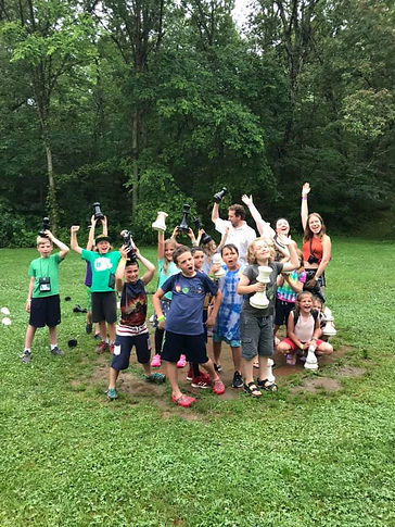 A large group of kids with their counselors holding up huge chess pieces from an outdoor game.