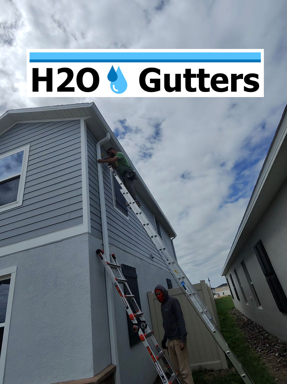 Eye-level view of crew installing a two-story downspout on a house exterior